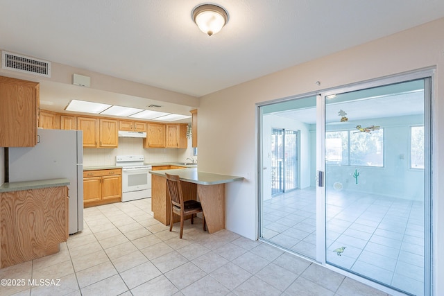 kitchen with tasteful backsplash, a kitchen breakfast bar, light tile patterned floors, kitchen peninsula, and white appliances