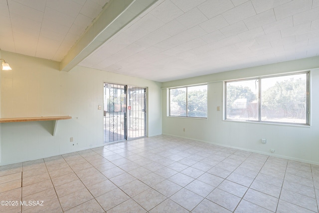 tiled spare room featuring beamed ceiling