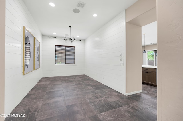 spare room with wooden walls and an inviting chandelier