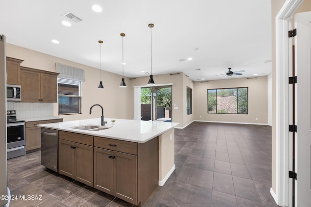 kitchen with sink, appliances with stainless steel finishes, an island with sink, decorative backsplash, and decorative light fixtures