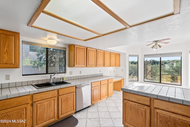 kitchen featuring sink, light tile patterned floors, stainless steel dishwasher, and tile counters