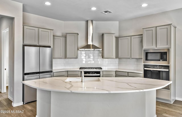 kitchen featuring appliances with stainless steel finishes, a center island with sink, and wall chimney range hood