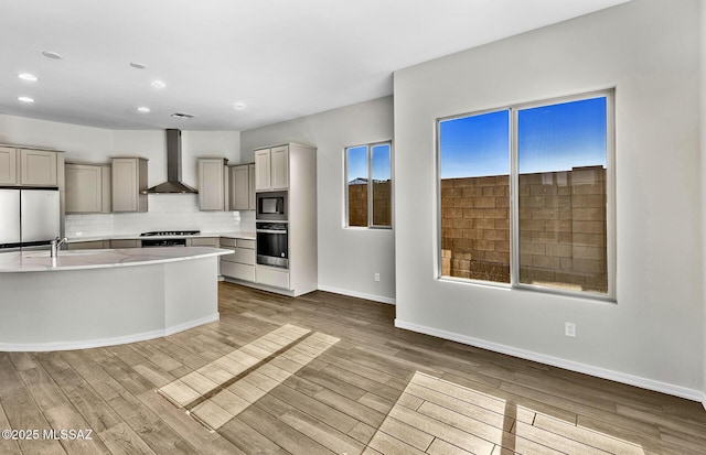 kitchen with fridge, gray cabinetry, stainless steel oven, and wall chimney exhaust hood