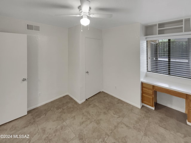 unfurnished room with ceiling fan and built in desk