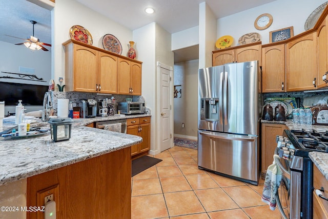 kitchen with light tile patterned floors, a toaster, decorative backsplash, appliances with stainless steel finishes, and light stone countertops