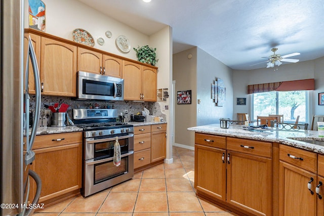 kitchen with light tile patterned floors, tasteful backsplash, ceiling fan, light stone counters, and stainless steel appliances