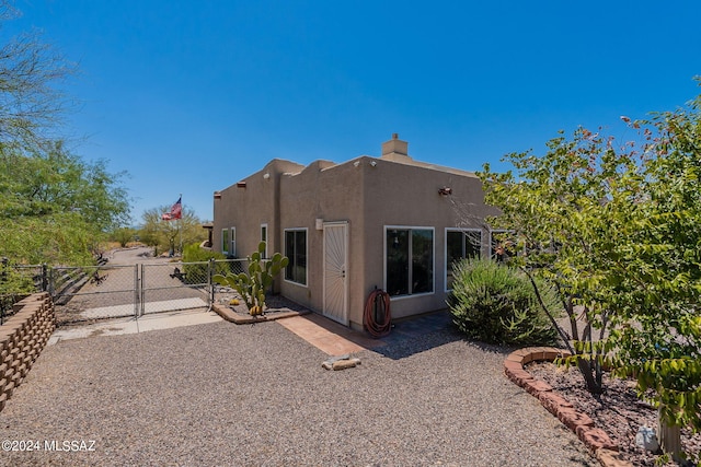 rear view of house with a chimney, a gate, fence, a patio area, and stucco siding