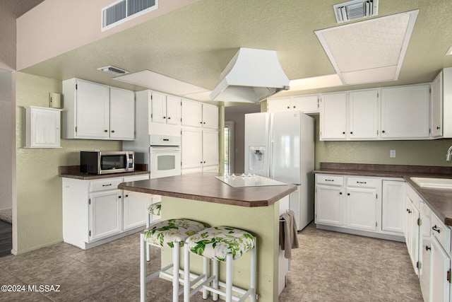 kitchen featuring white appliances, a kitchen bar, and white cabinetry