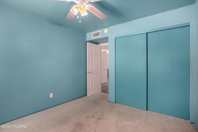 unfurnished bedroom with a closet, ceiling fan, carpet flooring, and a textured ceiling