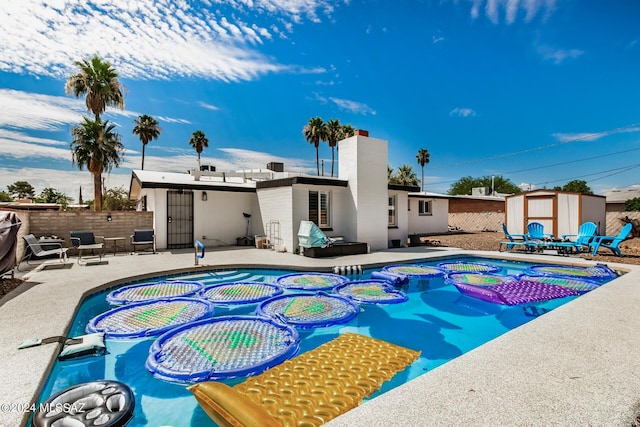 view of swimming pool featuring a patio, a storage unit, and an in ground hot tub