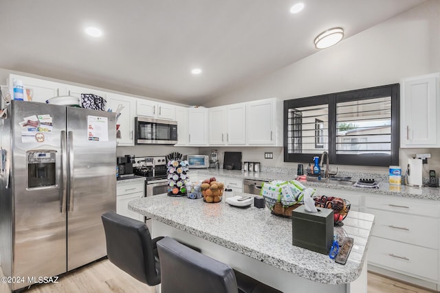 kitchen featuring stainless steel appliances, light hardwood / wood-style floors, white cabinets, and vaulted ceiling