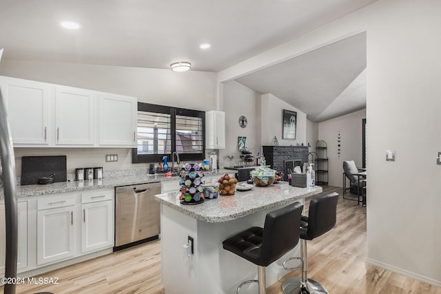 kitchen with light stone countertops, stainless steel dishwasher, light wood-type flooring, a breakfast bar area, and white cabinets