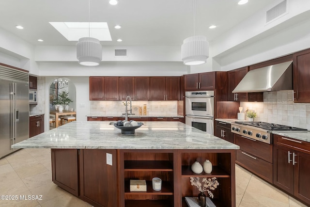 kitchen featuring pendant lighting, wall chimney exhaust hood, built in appliances, and a center island