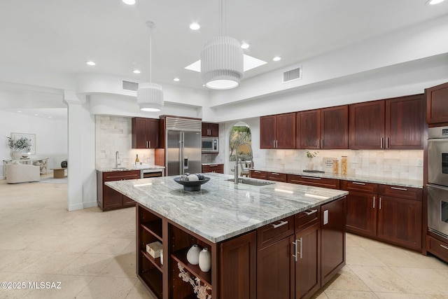 kitchen featuring sink, built in appliances, decorative light fixtures, a center island with sink, and light stone countertops