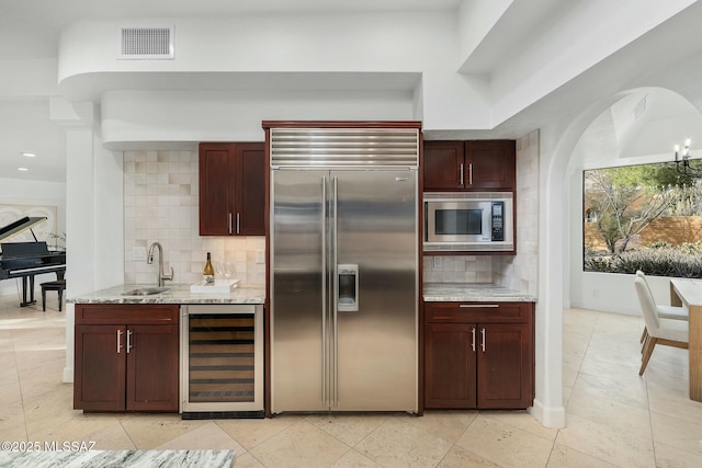 kitchen with sink, built in appliances, light stone counters, wine cooler, and tasteful backsplash