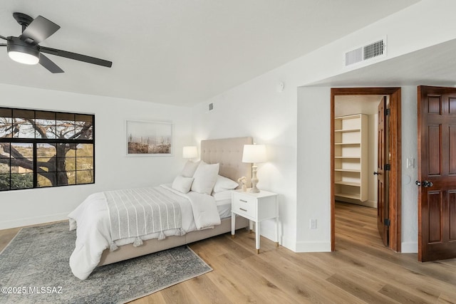 bedroom featuring a walk in closet, ceiling fan, and light wood-type flooring