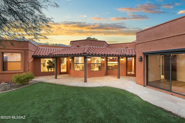 back house at dusk with a patio and a yard