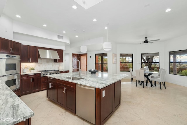 kitchen with pendant lighting, sink, appliances with stainless steel finishes, a kitchen island with sink, and wall chimney exhaust hood