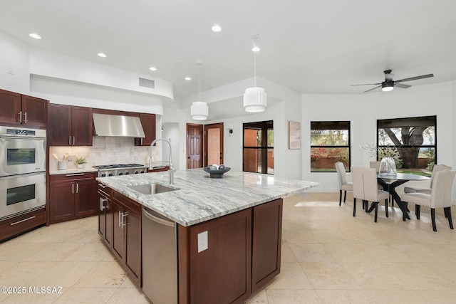 kitchen with hanging light fixtures, sink, a kitchen island with sink, and wall chimney exhaust hood