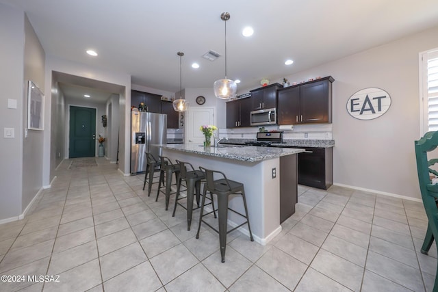 kitchen featuring appliances with stainless steel finishes, light stone counters, dark brown cabinets, a kitchen island with sink, and sink