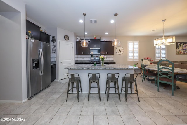 kitchen featuring an island with sink, a chandelier, pendant lighting, a breakfast bar, and appliances with stainless steel finishes