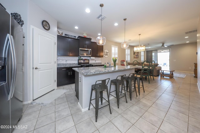 kitchen featuring a kitchen bar, appliances with stainless steel finishes, ceiling fan, decorative light fixtures, and a center island with sink