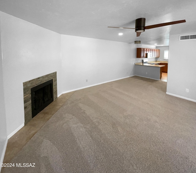 unfurnished living room with light carpet, ceiling fan, and a tiled fireplace