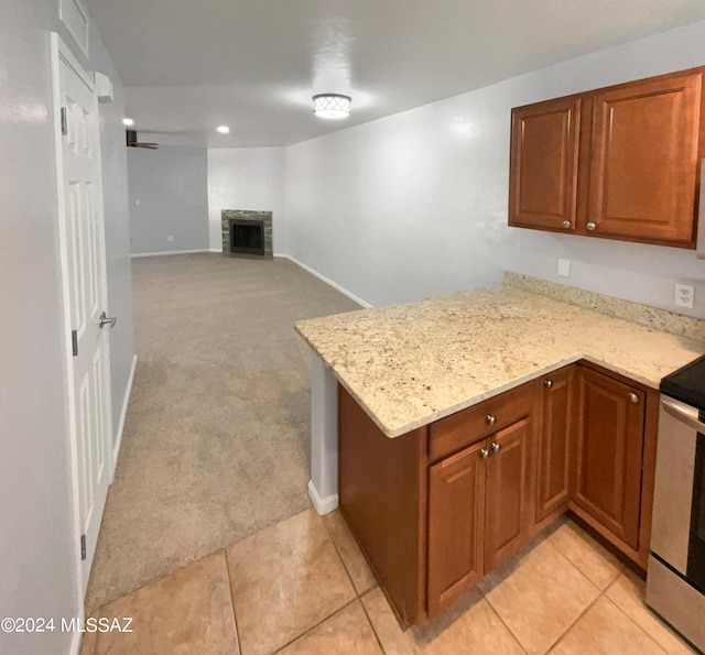 kitchen with stainless steel electric range, light carpet, a stone fireplace, light stone countertops, and kitchen peninsula