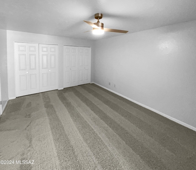 unfurnished bedroom featuring dark colored carpet, ceiling fan, and multiple closets