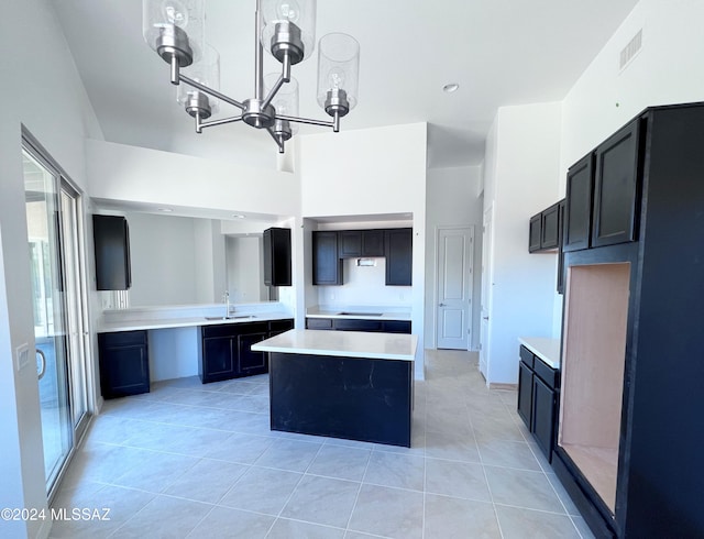 kitchen with sink, light tile patterned floors, stovetop, a chandelier, and a kitchen island