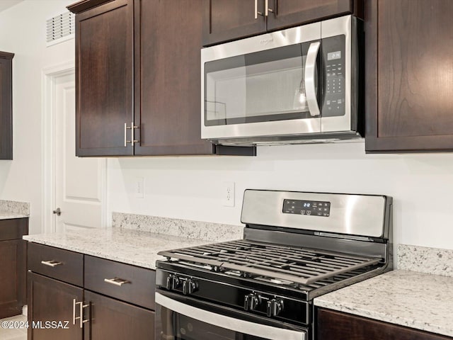 kitchen with appliances with stainless steel finishes, light stone countertops, and dark brown cabinetry