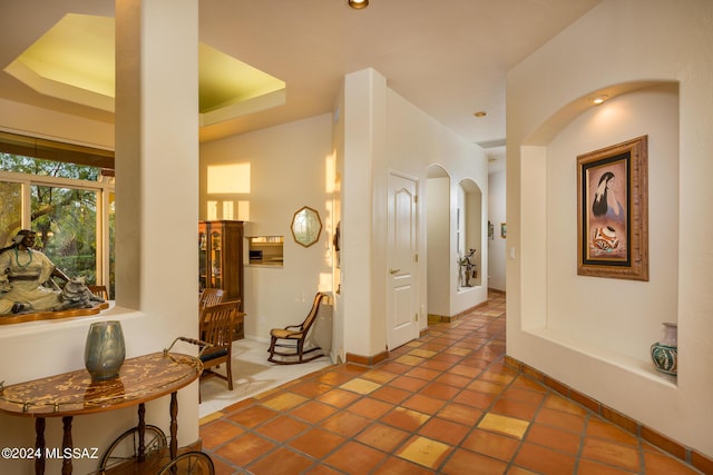 hall with a tray ceiling and tile patterned flooring