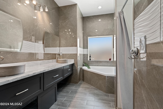 bathroom with tile walls, tiled tub, tile patterned floors, and vanity