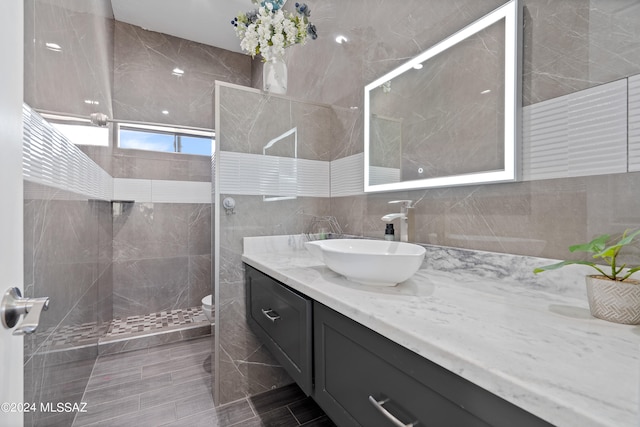 bathroom with a shower with shower door, toilet, vanity, tile walls, and tile patterned floors