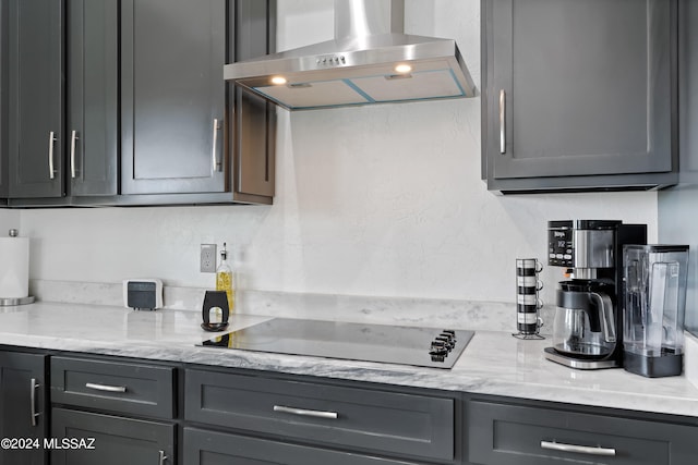 kitchen with gray cabinetry, light stone countertops, and wall chimney range hood