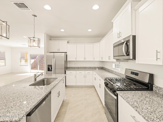 kitchen featuring stainless steel appliances, light stone countertops, pendant lighting, white cabinets, and sink