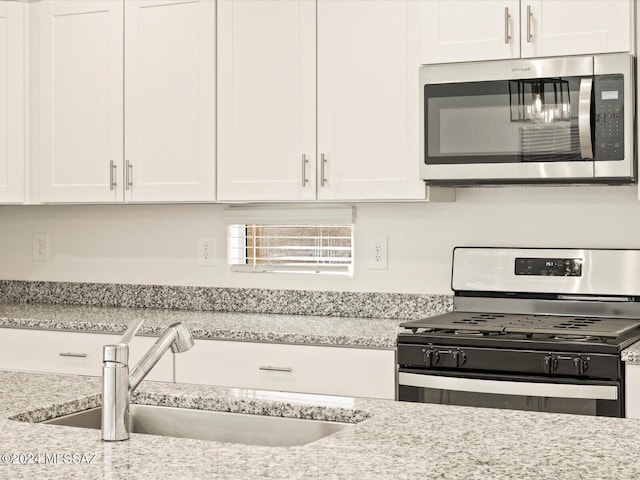 kitchen featuring appliances with stainless steel finishes, white cabinets, light stone countertops, and sink