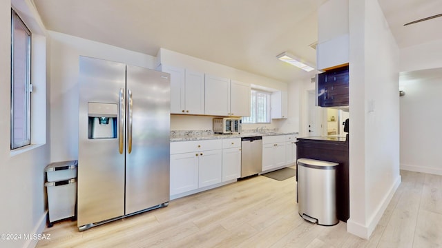 kitchen featuring light stone countertops, light wood-type flooring, white cabinetry, and stainless steel appliances