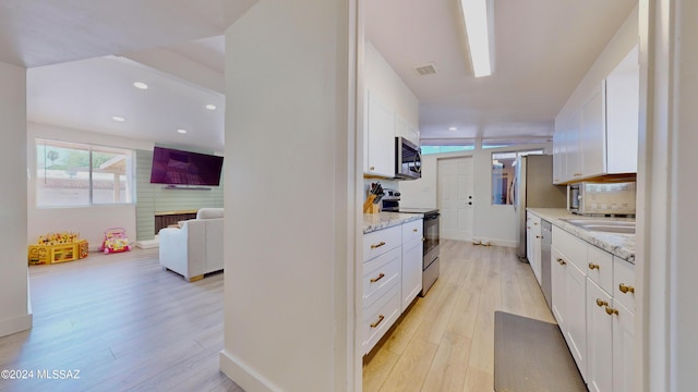 kitchen featuring light hardwood / wood-style flooring, light stone countertops, a fireplace, white cabinetry, and stainless steel appliances