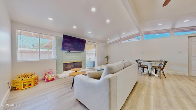 living room featuring vaulted ceiling with beams, plenty of natural light, light wood-type flooring, and a fireplace