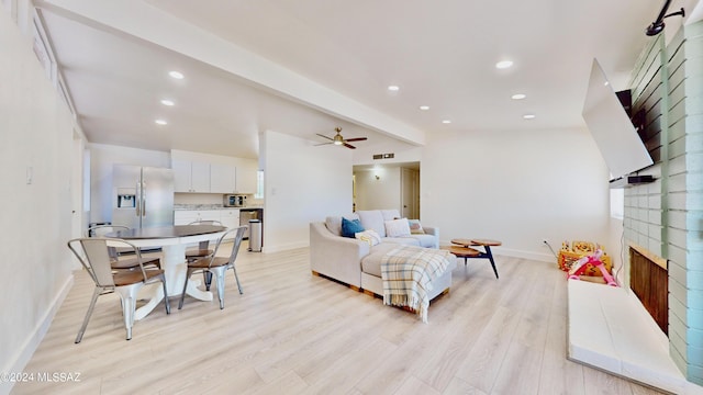 living room with beamed ceiling, ceiling fan, light hardwood / wood-style floors, and a brick fireplace