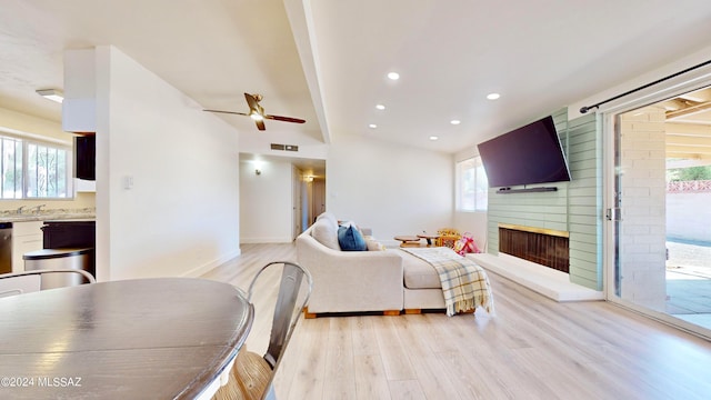 living room featuring a fireplace, light hardwood / wood-style floors, vaulted ceiling, and ceiling fan