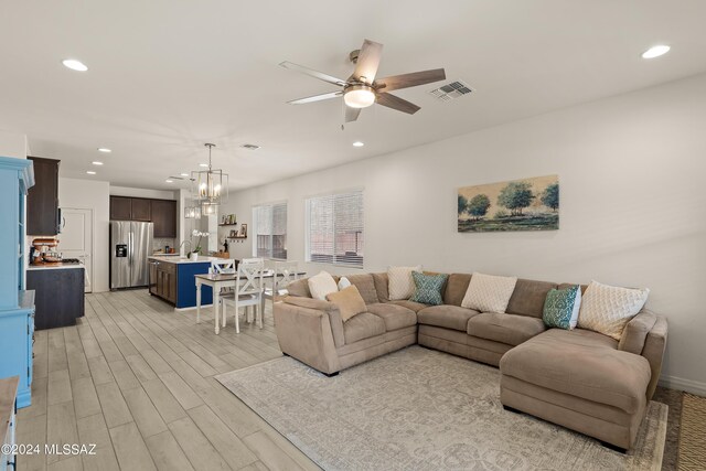 living room with light wood-type flooring and ceiling fan with notable chandelier