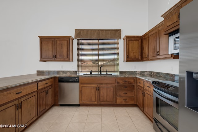 kitchen with light tile patterned flooring, dark stone counters, sink, kitchen peninsula, and appliances with stainless steel finishes