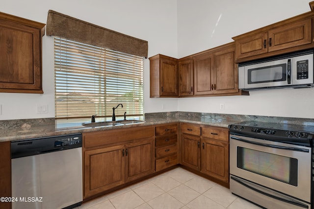 kitchen with appliances with stainless steel finishes, dark stone countertops, sink, and light tile patterned floors