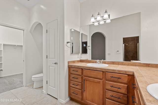 bathroom with tiled shower, vanity, tile patterned flooring, and toilet