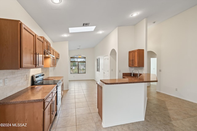 kitchen with light tile patterned floors, backsplash, a skylight, electric range, and kitchen peninsula