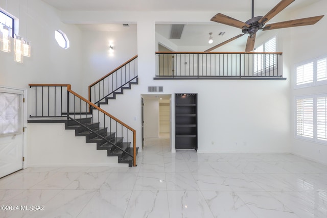 stairs with ceiling fan, a towering ceiling, and beam ceiling