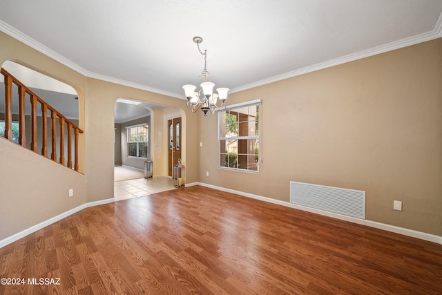 empty room with light hardwood / wood-style flooring, ornamental molding, and an inviting chandelier