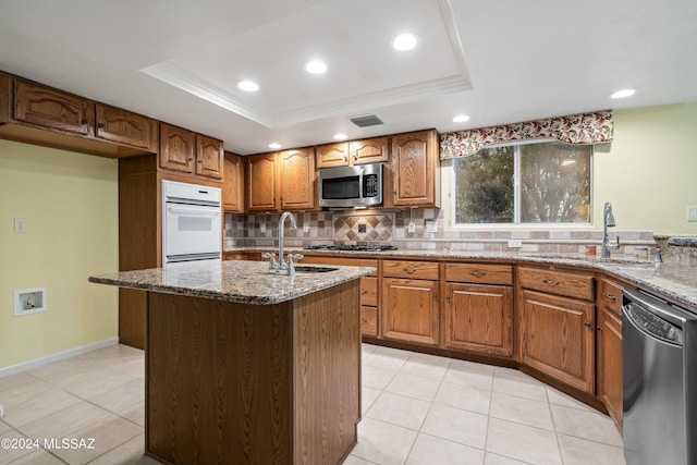 kitchen featuring sink, appliances with stainless steel finishes, stone countertops, and a tray ceiling